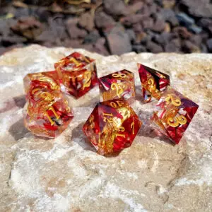 Set di sette dadi Power of the Ring: Dwarven Strength in resina rossa trasparente a spigoli vivi, numeri dorati, su roccia