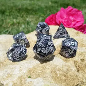 Set Moonwing Relics di sette dadi in resina nera a spigoli vivi con farfalle rosa e bianche e numeri argento su una roccia