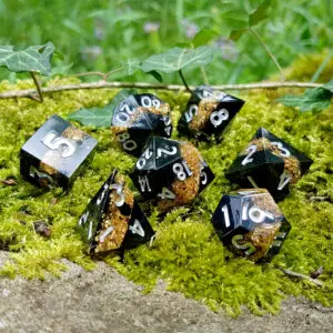 Set di sette dadi in resina a spigolo vivo Obsidian Shards: Golden Sand, neri con glitter oro e numeri argento sul muschio