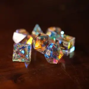 Set di sette dadi poliedrici Aurora Shard in vetro trasparente con riflessi arcobaleno e numeri dorati su un tavolo di legno