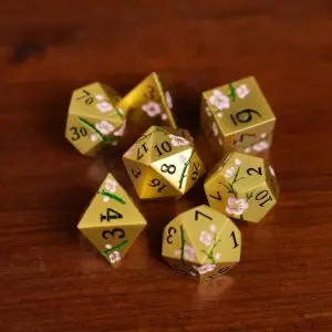 Set di dadi in metallo Golden Sakura: sette dadi poliedrici dorati con numeri neri e rami di ciliegio rosa su legno