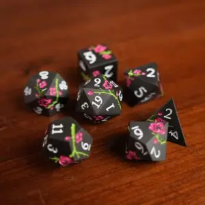 Set di dadi in metallo Dark Sakura: sette dadi poliedrici neri opachi con fiori di ciliegio rosa, rami verdi e numeri bianchi