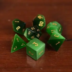 Set di sette dadi poliedrici Tiger's Gaze in pietra occhio di gatto verde con numeri gotici dorati su un tavolo di legno