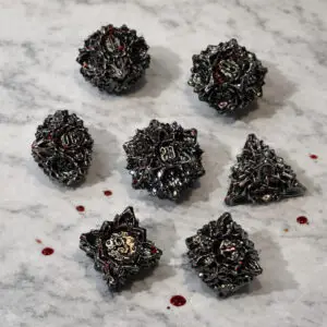 Set di dadi in metallo Bloody Rose: sette dadi poliedrici neri a forma di rosa con accenti rossi su marmo bianco con gocce rosse
