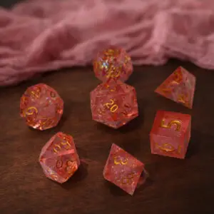 Set di sette dadi Blossom Crystals in resina rosa a spigoli vivi, numeri dorati e scaglie iridescenti su tavolo in legno