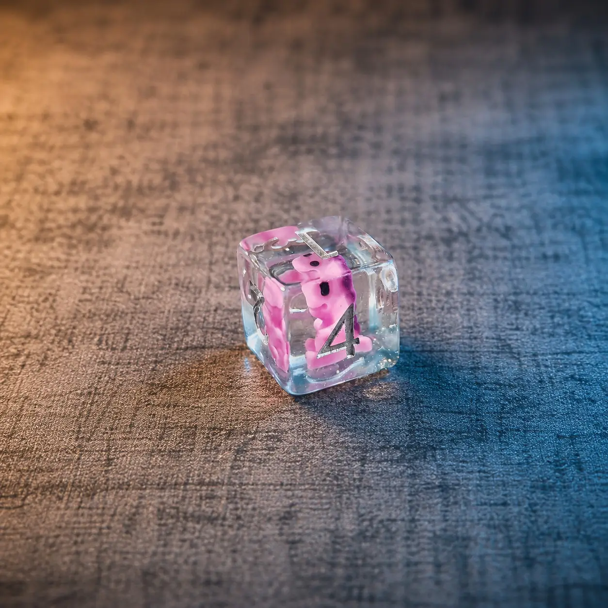 The Pink Menace – Set di Dadi in Resina con Miniature 4 D6 del set The Pink Menace: dado in resina trasparente con miniatura rosa all'interno e numeri argentati su fondo grigio