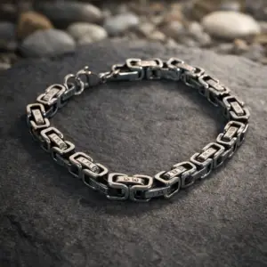 The Warden Runes' Oath silver metal chain bracelet with rune-engraved links and lobster clasp on a grey stone