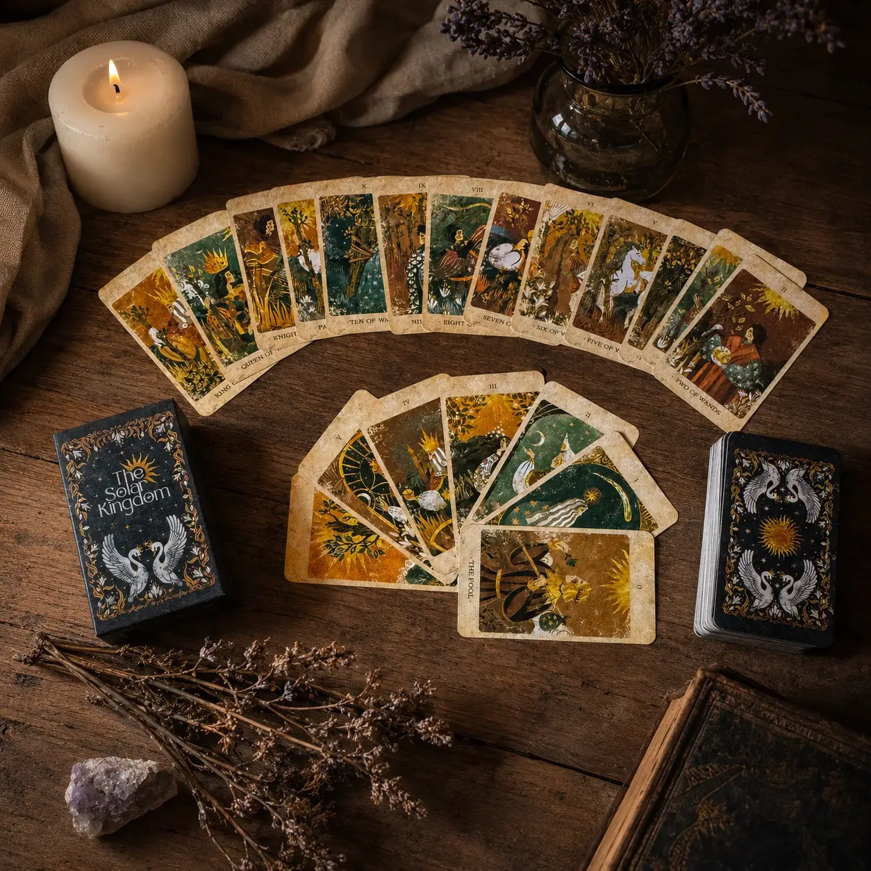 Carte Solar Kingdom Tarot a ventaglio su tavolo di legno con scatola nera con cigni e sole, mazzo, candela e lavanda secca